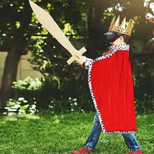 Young boy in a royal red costume cape and golden crown playing in a green garden