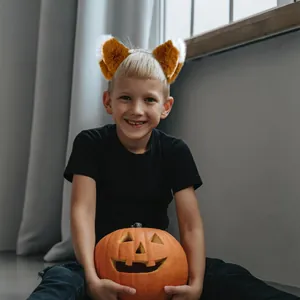 Adorable child wearing a fluffy fox ear headband while holding a Halloween pumpkin lantern