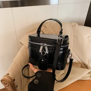 Sac à main boîte noir élégant et minimaliste avec poignée et bandoulière réglable.