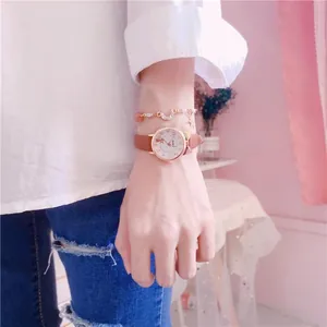 Close-up of a stylish pink leather strap girl's watch worn with a charm bracelet.