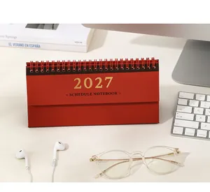 Nahaufnahme eines roten 2027 Spiral-Tischkalenders auf einem modernen weißen Schreibtisch