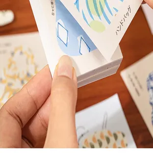 Gros plan d'une main feuilletant un carnet d'autocollants esthétiques épais et inscriptibles.