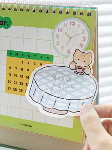 Close-up of a cute cartoon cat sticky note featuring handwritten Chinese text on a calendar