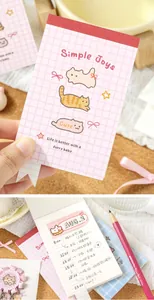 Close-up of cute cat mini notepad showing handwritten daily schedule and a pink pencil