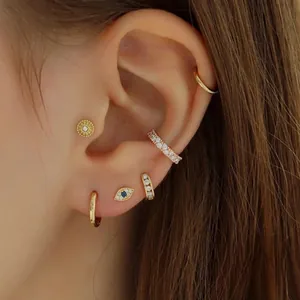 Detailed close-up view of gold evil eye earring set with blue crystals on a human ear.