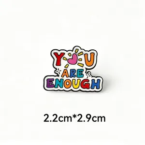 Macro view of colorful 'YOU ARE ENOUGH' enamel pin badge showing exact 2.2cm x 2.9cm size info