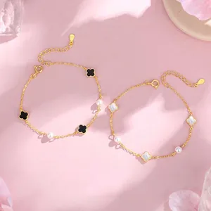 Primer plano de pulseras de trébol doradas con perlas y esmalte sobre fondo rosa