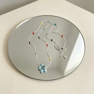 Collar de cuentas de colores con colgante de flor azul claro sobre un espejo redondo