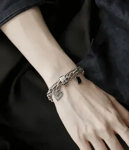 Dettaglio di un bracciale vintage multistrato con ciondoli a cuore e croce al polso.