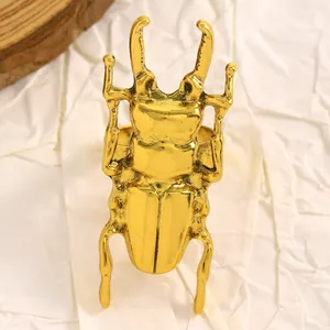 Dettaglio macro di un orecchino dorato a forma di scarabeo con finitura vintage strutturata.