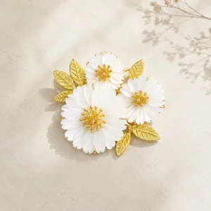 Detailed view of a white daisy brooch with golden leaves on a textured cream surface