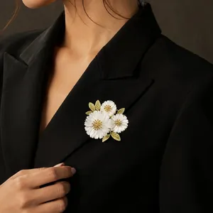 Elegant white daisy floral brooch featuring gold leaves pinned on a black blazer lapel