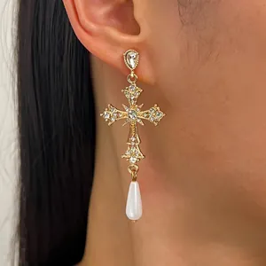 Primo piano di orecchino a croce gotica dorata con cristalli e goccia di perla bianca