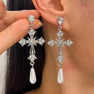 Dettaglio di orecchini a croce gotica decorati con strass e perla bianca pendente