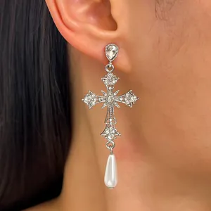 Primo piano di orecchino a croce gotica argento con strass e ciondolo di perla