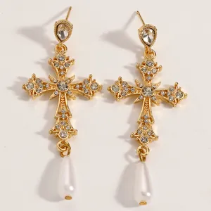 Dettaglio di orecchini a croce gotica dorati con pendenti a perla a goccia.