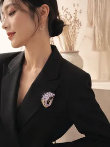 Vista dettagliata di un'elegante spilla a pavone in cristallo viola sul bavero di un blazer nero.
