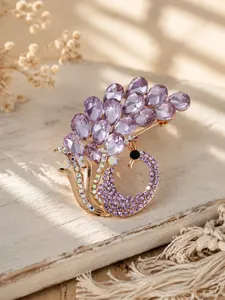 Primo piano di un'elegante spilla a pavone in cristallo viola su una superficie di legno