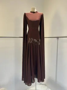 Prachtig detail van bruine avondjurk met kralenborduursel en elegante cape-mouwen.