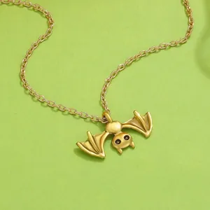 Detailed close-up of a punk style gold-colored bat pendant necklace on green background