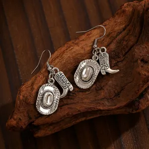 Close-up of vintage silver Western cowboy hat and boot charm earrings on wood
