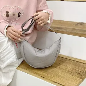 Detail view of a light gray nylon dumpling bag held by a model in a casual setting.