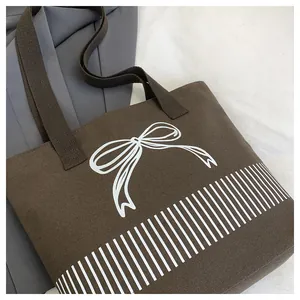 Detailaufnahme einer braunen Canvas-Tasche mit weißem Schleifen-Design und Streifenmuster.