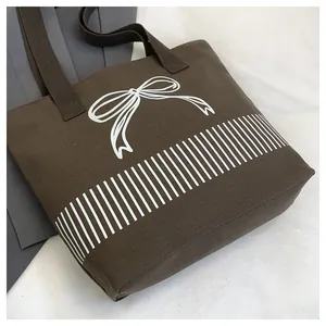 Detail einer braunen Canvas-Einkaufstasche mit weißem Schleifendesign und Streifen.