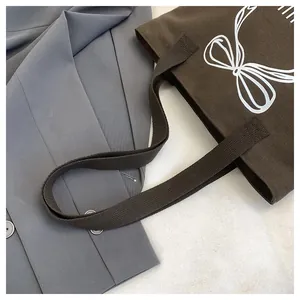 Detailansicht der braunen Canvas-Einkaufstasche mit weißem Schleifenmuster auf grauem Blazer