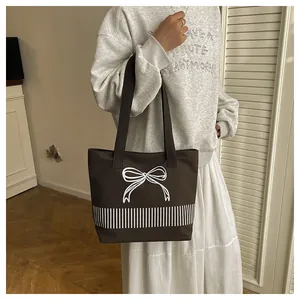 Nahaufnahme eines Modells mit einer braunen Canvas-Tasche mit weißer Schleife und Streifen