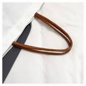 Close-up view of brown leather-like handles on a white minimalist canvas tote bag.