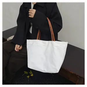 Close-up of a stylish white canvas tote bag with brown handles carried by a model