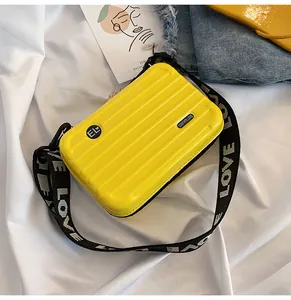Detailaufnahme einer gelben Mini-Koffertasche zum Umhängen mit schwarzem „LOVE“-Gurt.