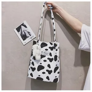 Détail du sac cabas en toile à motif vache avec charm ours et écusson de marque Augur