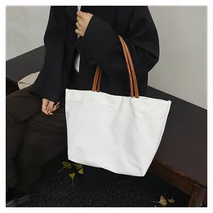 Close-up view of a minimalist white canvas tote bag with brown straps held by a model