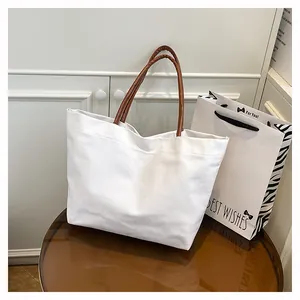 Detailed view of a large white canvas tote bag with brown handles on a stylish table