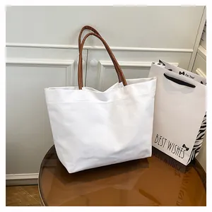 Large white minimalist canvas tote bag with stylish brown leather handles shown on a table
