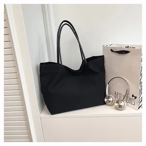 Minimalist black canvas tote bag in a lifestyle setting with headphones and gift bag