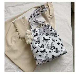 Vue détaillée du sac fourre-tout blanc avec imprimé papillon noir et breloque ours.