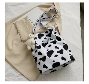 Vue détaillée d'un sac cabas en toile à motif vache avec un porte-clés ours en peluche
