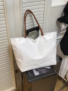 Large white canvas tote bag with brown leather handles on a suitcase travel scene