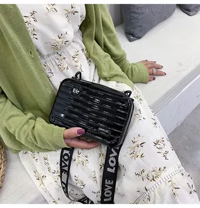 Detailansicht einer glänzend schwarzen Mini-Koffer Umhängetasche auf blumigem Kleid.