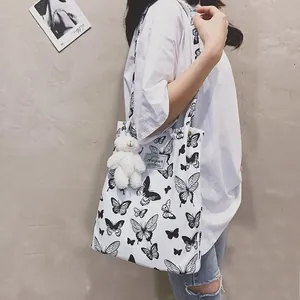 Borsa tote in tela bianca con stampa a farfalla, ciondolo a orsetto e tracolla.