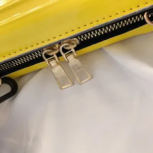 Detailansicht einer leuchtend gelben Lackleder-Mini-Box-Tasche mit goldenen Reißverschlüssen.
