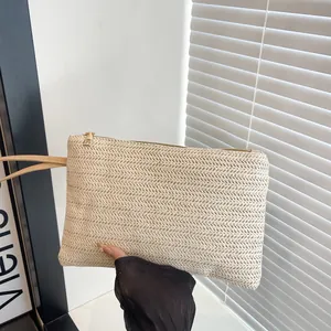 Close-up detail of a minimalist beige straw woven clutch bag held by hand for vacation