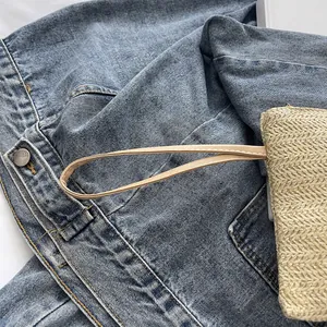 Detail view of a woven straw beach wristlet bag with a tan leather strap