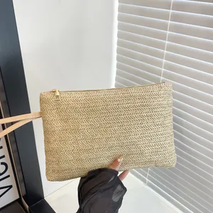 Close-up of minimalist beige woven straw clutch bag with gold zipper and wrist strap