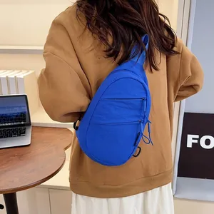 Model wearing a vibrant blue nylon crossbody chest bag in a lifestyle setting.