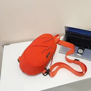 Detailed view of a vibrant orange nylon sling bag placed on a minimalist desk workspace