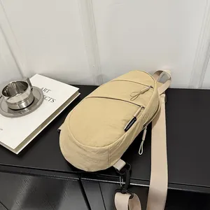 Angled detail view of a beige nylon casual chest bag featuring dual zipper compartments.